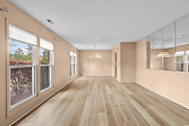 unfurnished room featuring visible vents, an inviting chandelier, baseboards, and light wood-type flooring