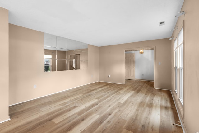 empty room with wood finished floors, visible vents, and baseboards