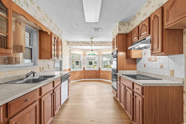 kitchen with wallpapered walls, under cabinet range hood, black appliances, a sink, and a textured ceiling