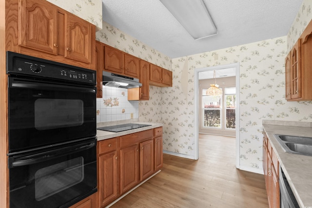 kitchen with under cabinet range hood, brown cabinetry, black appliances, light wood-style flooring, and wallpapered walls