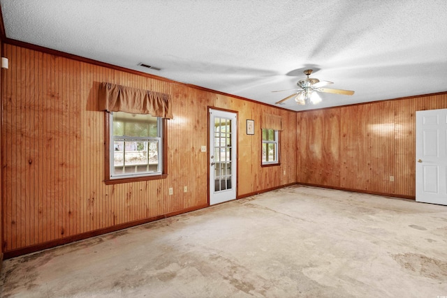 carpeted spare room with ceiling fan, wood walls, ornamental molding, and a textured ceiling