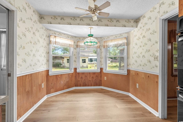 unfurnished dining area featuring light wood finished floors, ceiling fan, wainscoting, and a healthy amount of sunlight