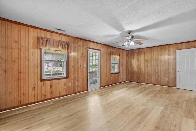 spare room featuring wood finished floors, wood walls, ornamental molding, visible vents, and a ceiling fan