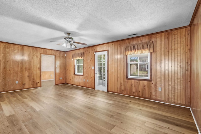 empty room with visible vents, hardwood / wood-style flooring, ceiling fan, and wood walls