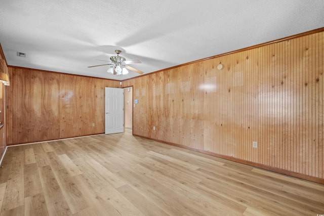 spare room featuring a textured ceiling, visible vents, wooden walls, wood finished floors, and a ceiling fan
