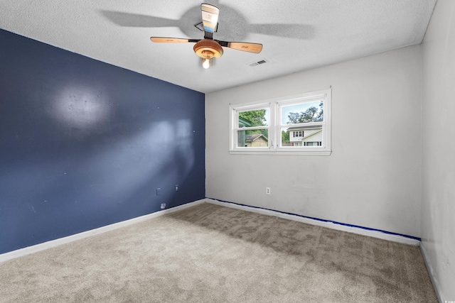carpeted empty room featuring a textured ceiling, visible vents, a ceiling fan, and baseboards