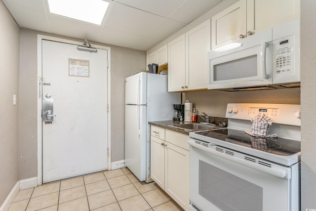 kitchen with a paneled ceiling, white appliances, sink, light tile patterned floors, and white cabinets