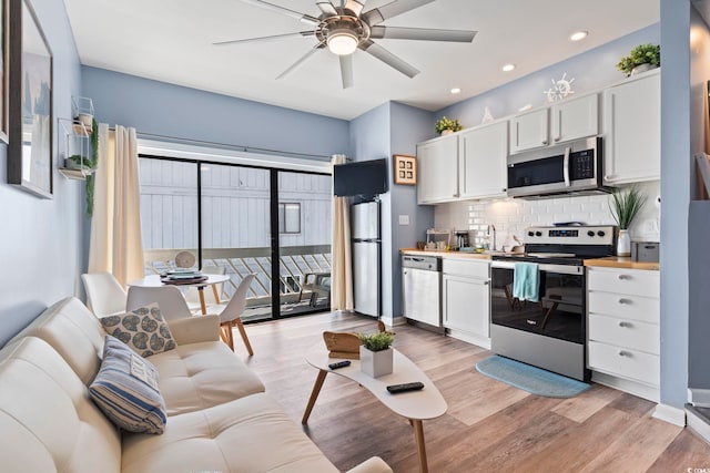 kitchen with light hardwood / wood-style flooring, ceiling fan, appliances with stainless steel finishes, tasteful backsplash, and white cabinetry