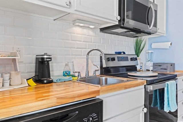 kitchen with appliances with stainless steel finishes, backsplash, white cabinetry, and butcher block counters