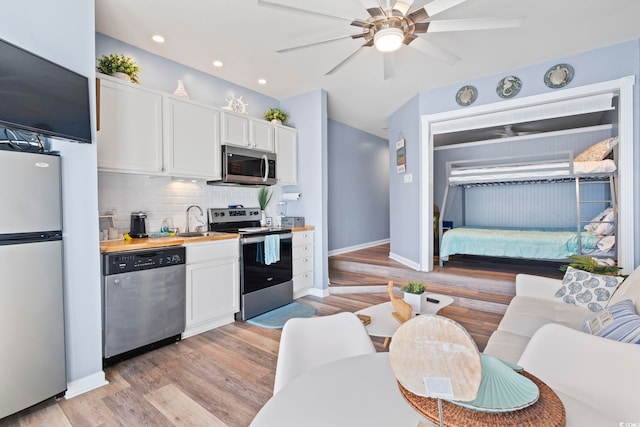 kitchen with decorative backsplash, appliances with stainless steel finishes, sink, light hardwood / wood-style flooring, and white cabinetry