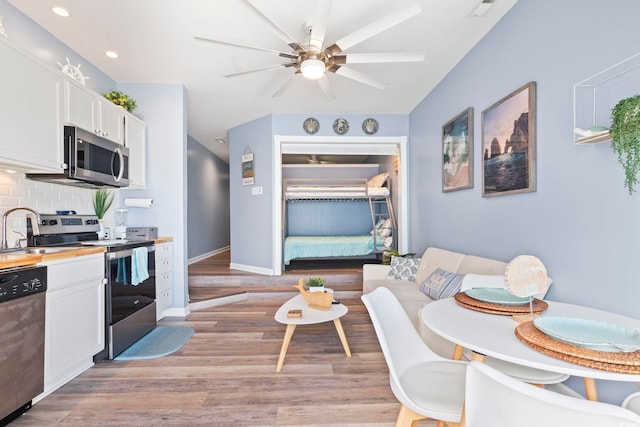 kitchen with decorative backsplash, appliances with stainless steel finishes, sink, light hardwood / wood-style floors, and white cabinetry