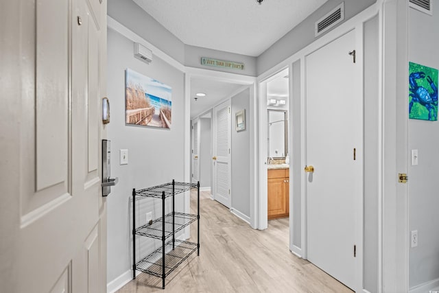 corridor with a textured ceiling and light hardwood / wood-style flooring