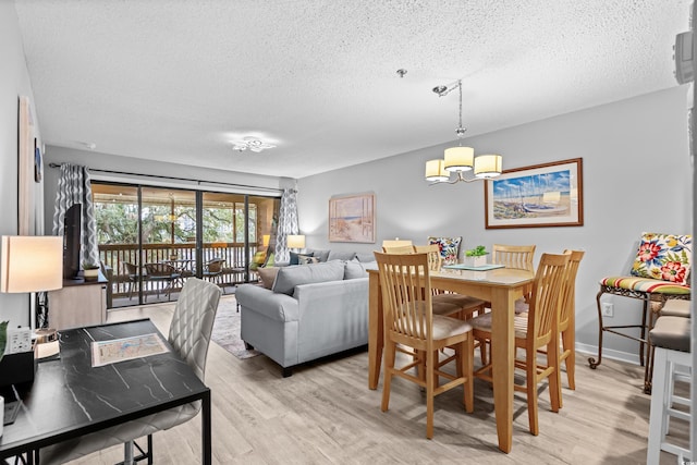 dining space with a textured ceiling, light hardwood / wood-style floors, and an inviting chandelier