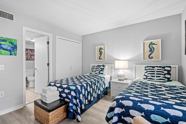 bedroom featuring light hardwood / wood-style floors, a textured ceiling, a closet, and ensuite bath