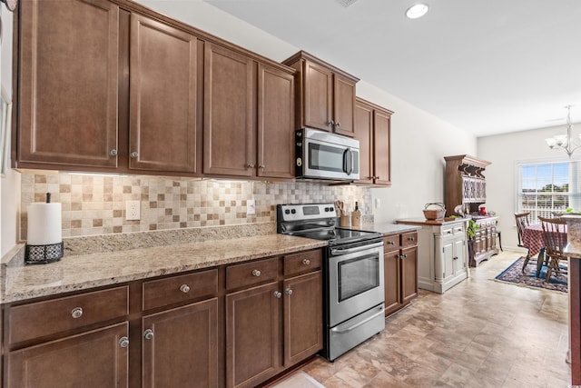 kitchen with light stone countertops, appliances with stainless steel finishes, backsplash, dark brown cabinetry, and a chandelier