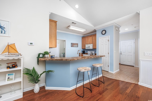 kitchen featuring a kitchen breakfast bar, kitchen peninsula, light hardwood / wood-style floors, lofted ceiling, and white appliances