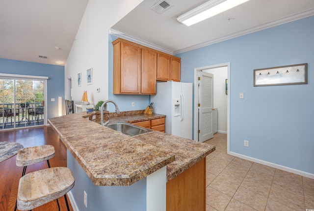 kitchen with kitchen peninsula, a breakfast bar, sink, white fridge with ice dispenser, and lofted ceiling