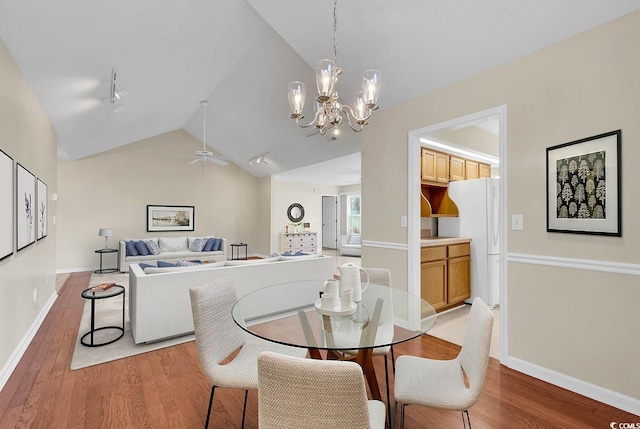 dining area with ceiling fan with notable chandelier, vaulted ceiling, and light wood-type flooring