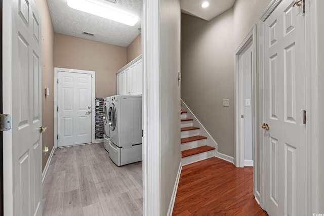 clothes washing area with a textured ceiling, cabinets, washing machine and dryer, and light hardwood / wood-style floors