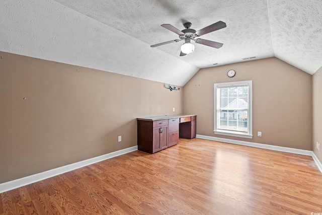 bonus room featuring light wood-type flooring, a textured ceiling, vaulted ceiling, and ceiling fan