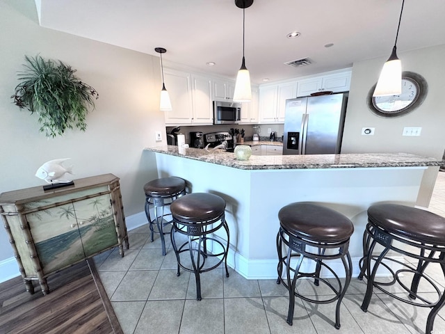 kitchen with stone counters, white cabinets, hanging light fixtures, appliances with stainless steel finishes, and kitchen peninsula