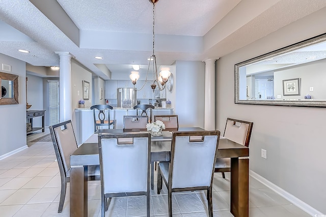 dining area featuring ornate columns, a textured ceiling, a tray ceiling, light tile patterned floors, and a chandelier