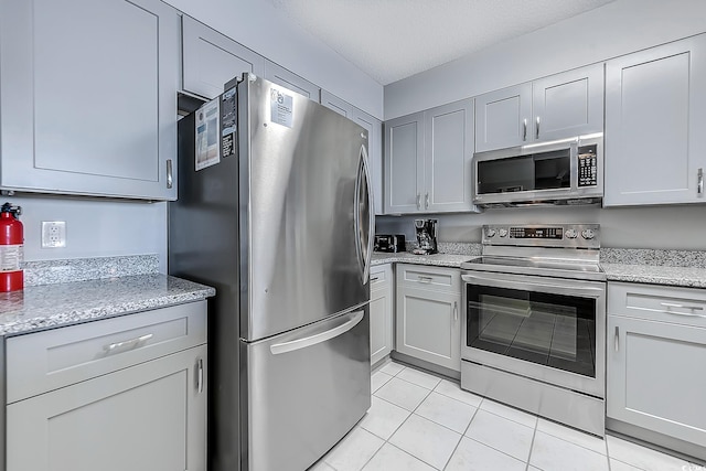 kitchen with light stone countertops, appliances with stainless steel finishes, a textured ceiling, light tile patterned floors, and gray cabinets