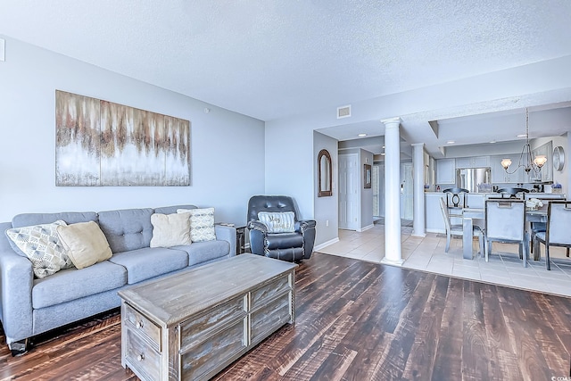 living room featuring a textured ceiling, hardwood / wood-style flooring, ornate columns, and a notable chandelier