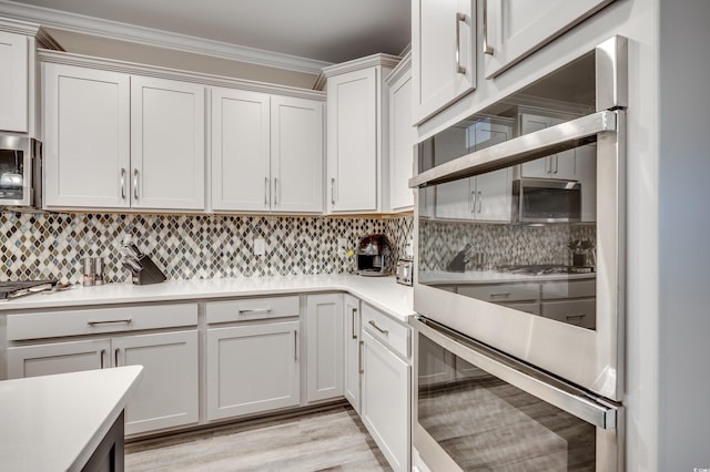 kitchen featuring crown molding, stainless steel appliances, tasteful backsplash, light countertops, and light wood-style flooring