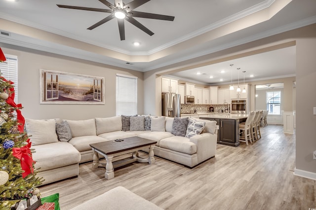 living area with recessed lighting, a raised ceiling, light wood-style floors, ornamental molding, and ceiling fan