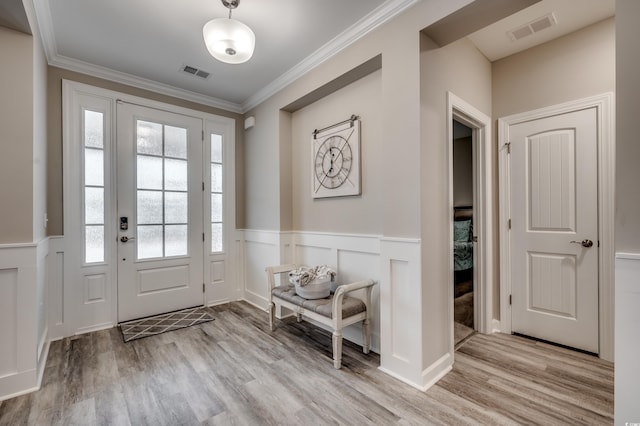 foyer with a wainscoted wall, visible vents, crown molding, and wood finished floors