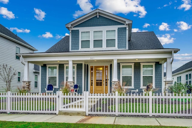 craftsman inspired home featuring covered porch, roof with shingles, and a fenced front yard