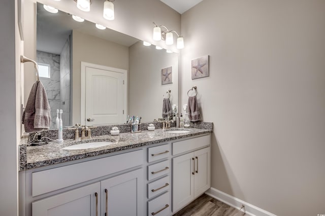 full bath with double vanity, wood finished floors, a sink, and baseboards