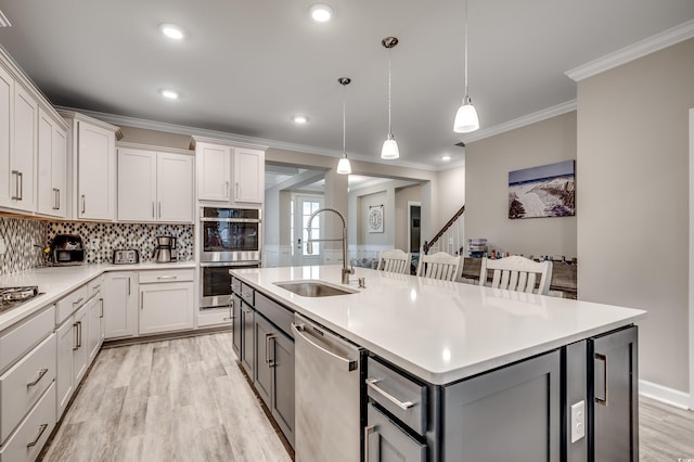 kitchen with a center island with sink, light countertops, gray cabinets, stainless steel appliances, and a sink