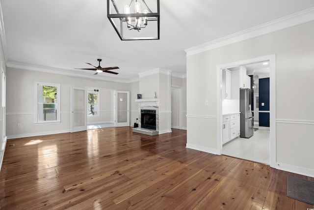 unfurnished living room featuring hardwood / wood-style flooring, ceiling fan with notable chandelier, and crown molding