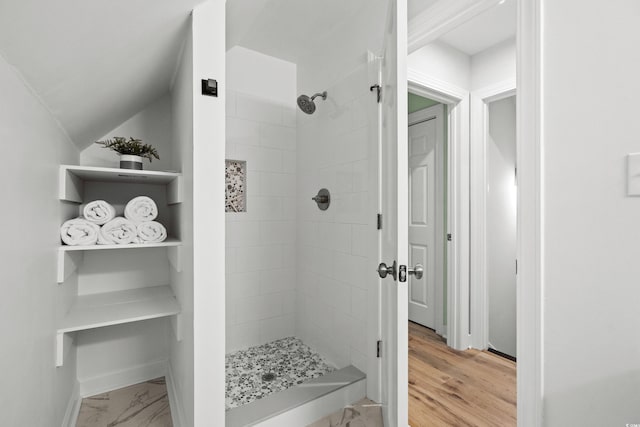 bathroom featuring hardwood / wood-style floors, a tile shower, and vaulted ceiling