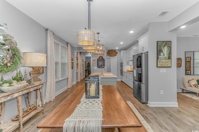 kitchen featuring a center island with sink, appliances with stainless steel finishes, hanging light fixtures, light countertops, and white cabinetry