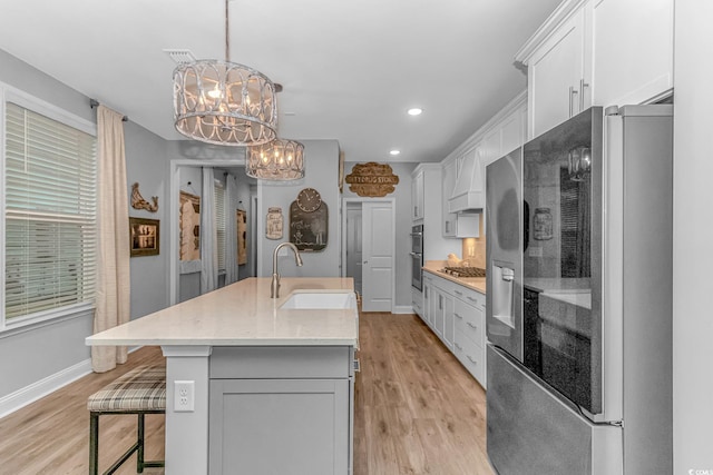 kitchen with decorative light fixtures, a center island with sink, appliances with stainless steel finishes, white cabinetry, and a sink