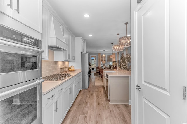 kitchen featuring white cabinetry, decorative light fixtures, stainless steel appliances, light hardwood / wood-style floors, and decorative backsplash