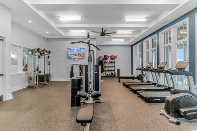 gym featuring ceiling fan, brick wall, and a tray ceiling