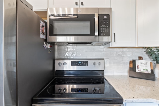 kitchen featuring white cabinets, backsplash, stainless steel appliances, and light stone countertops