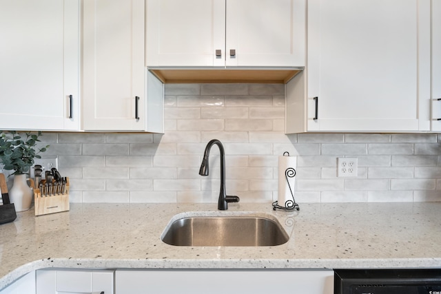 kitchen with light stone counters, white cabinetry, and sink