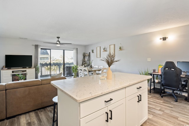 kitchen with light stone countertops, ceiling fan, white cabinets, a center island, and light hardwood / wood-style floors