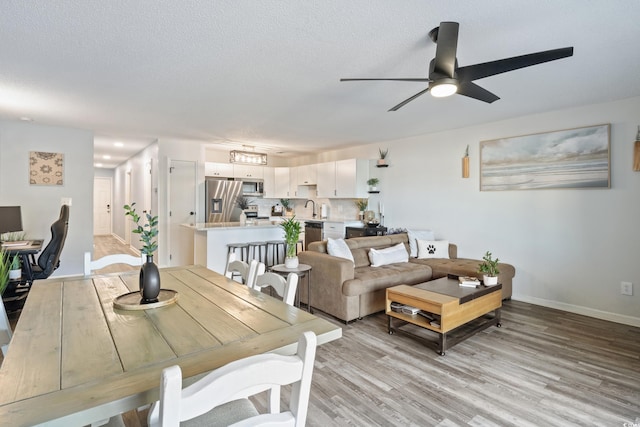 dining area featuring a textured ceiling, light hardwood / wood-style floors, ceiling fan, and sink