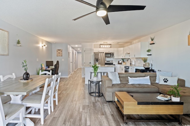 living room with a textured ceiling, light hardwood / wood-style flooring, ceiling fan, and sink