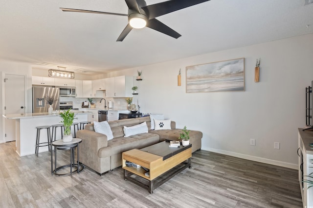 living room featuring light wood-type flooring, ceiling fan, and sink