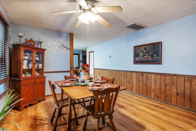 dining space featuring ceiling fan, light hardwood / wood-style flooring, wood walls, and a textured ceiling