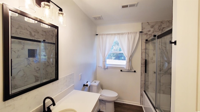 full bathroom with hardwood / wood-style flooring, toilet, combined bath / shower with glass door, and vanity