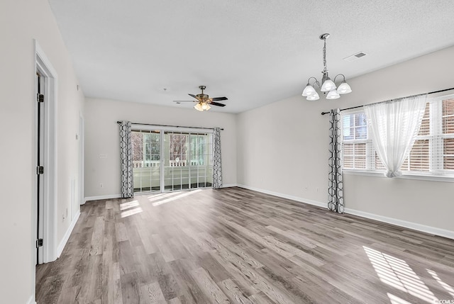 spare room featuring plenty of natural light, ceiling fan with notable chandelier, a textured ceiling, and light wood-type flooring