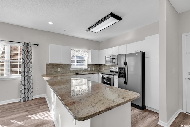 kitchen with sink, stone counters, appliances with stainless steel finishes, white cabinets, and kitchen peninsula